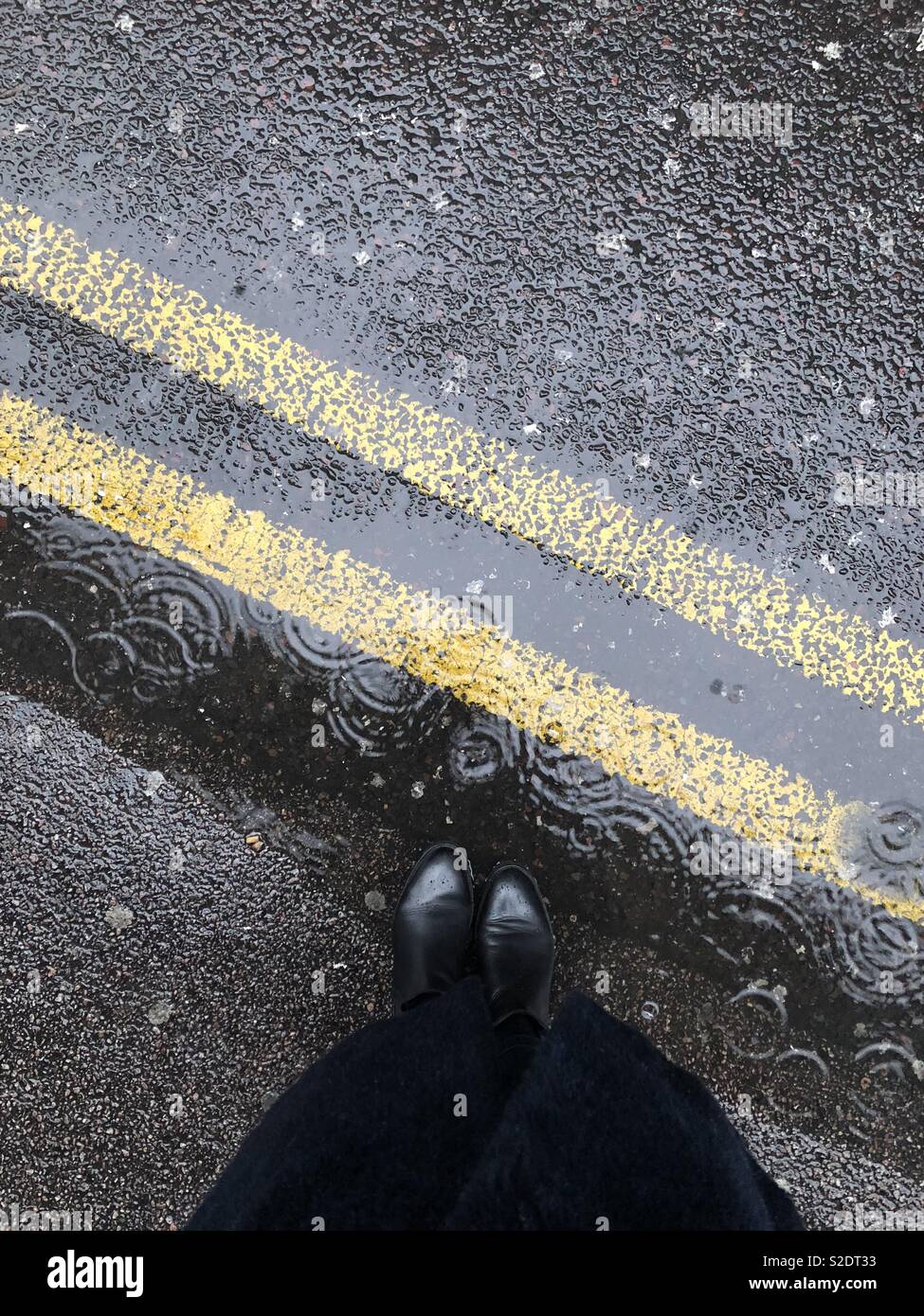 Bottes en cuir noir sous la pluie sur la double ligne jaune signalisation Banque D'Images