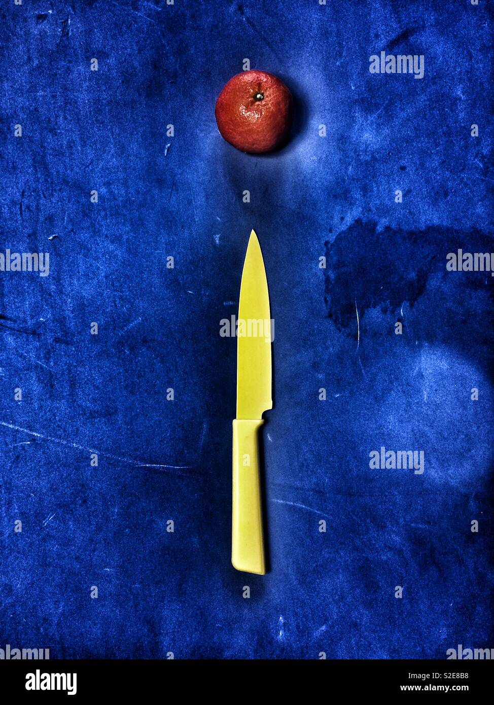Le couteau et la mandarine jaune sur fond bleu Banque D'Images