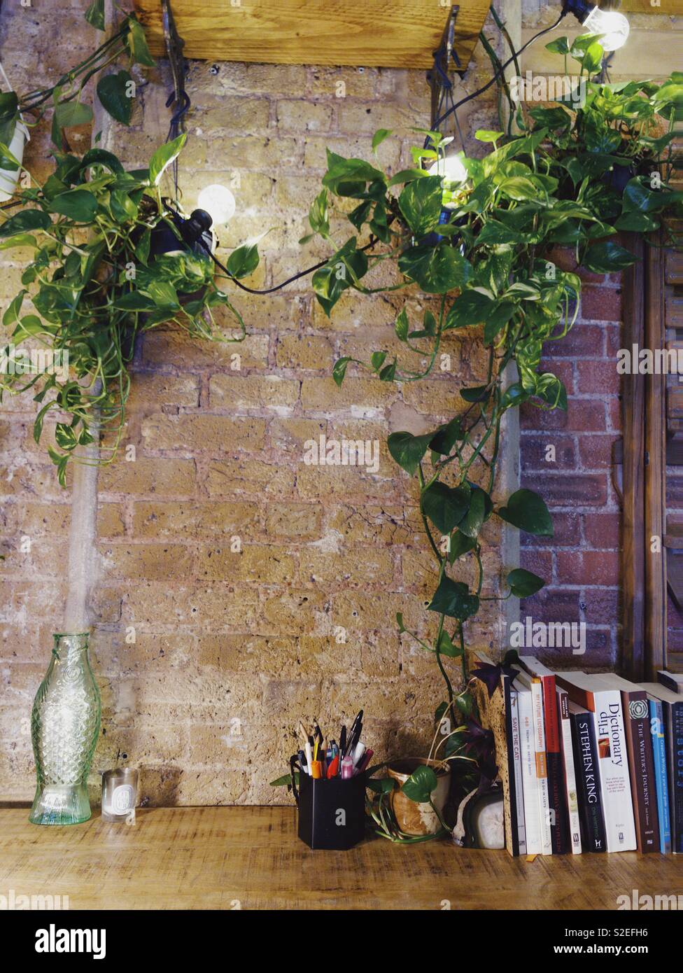 Bureau en bois d'écrivains couleur pierre contre mur en briques apparentes et de murs en briques rouges en bois lierre devils en retrait vers le bas. Ampoule navette fairy lights s'entremêlent avec les feuilles. L Banque D'Images