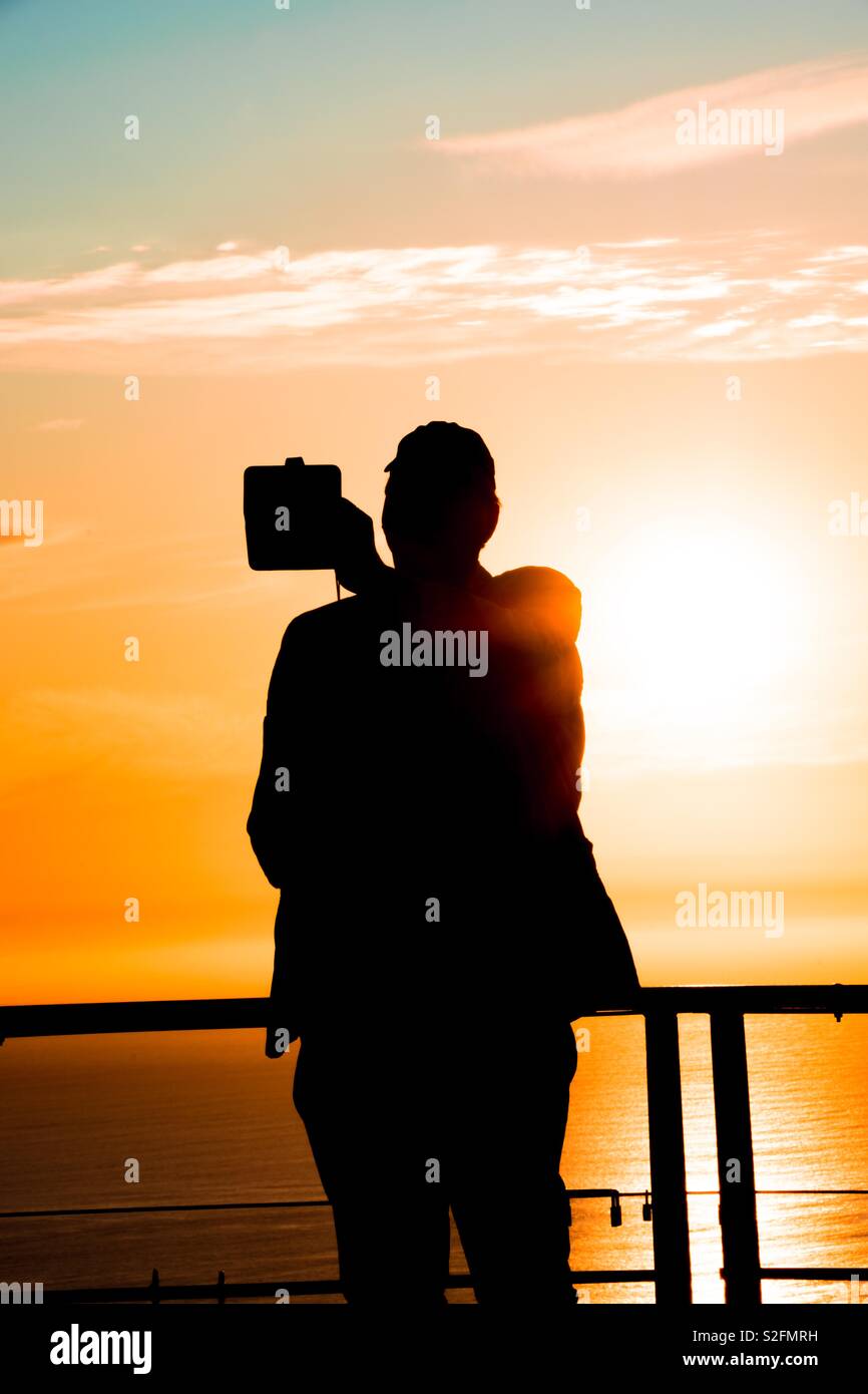 Silhouette de grand homme trapu de prendre au coucher du soleil sur selfies Signal Hill à Cape Town, Afrique du Sud Banque D'Images