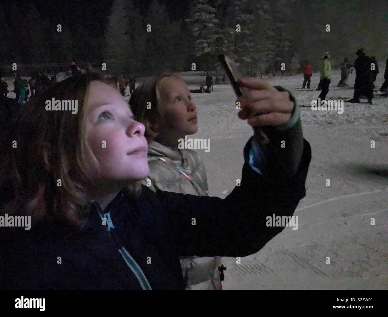Deux filles regarder un spectacle de lumière nocturne sur une pente de ski. L'un enregistre avec son smartphone et est éclairé par l'écran. - Image de stock capturée avec un smartphone