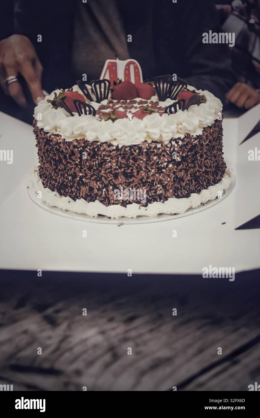 40e anniversaire - Gâteau au chocolat avec glaçage blanc et fraises - être coupé par une femme. Banque D'Images