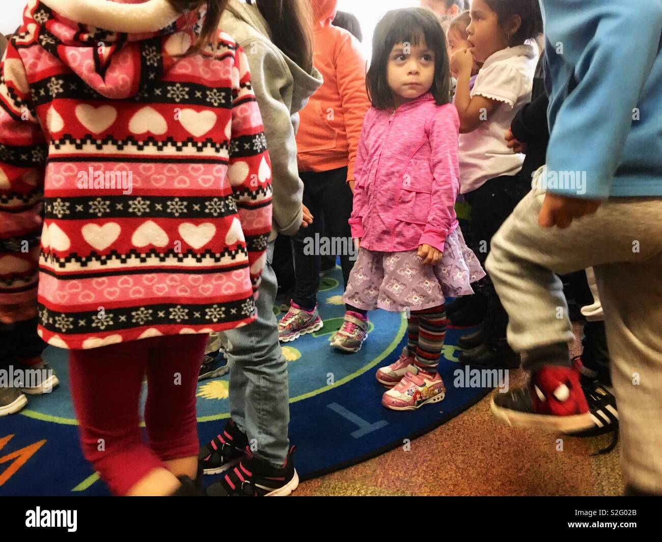 La preschool girl donne son attention à regarder quelqu'un alors que l'histoire de la bibliothèque de temps debout pour une pause. Banque D'Images