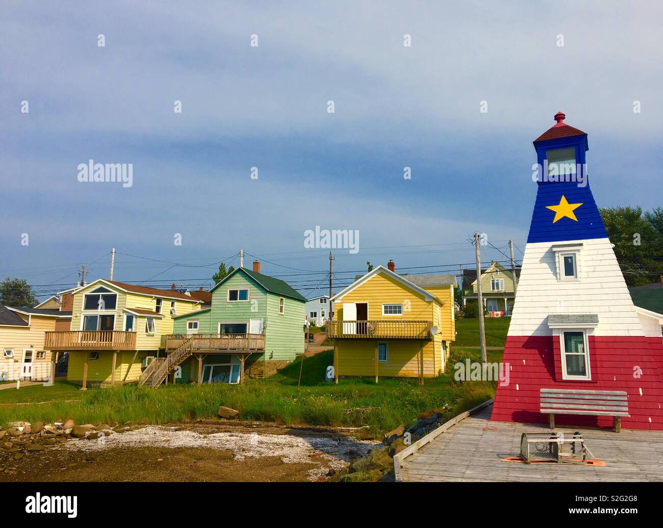 Peu de phare avec drapeau arcadienne peint sur elle avec des maisons de bord de l'île du Cap-Breton à Chéticamp Canada - Image de stock capturée avec un smartphone