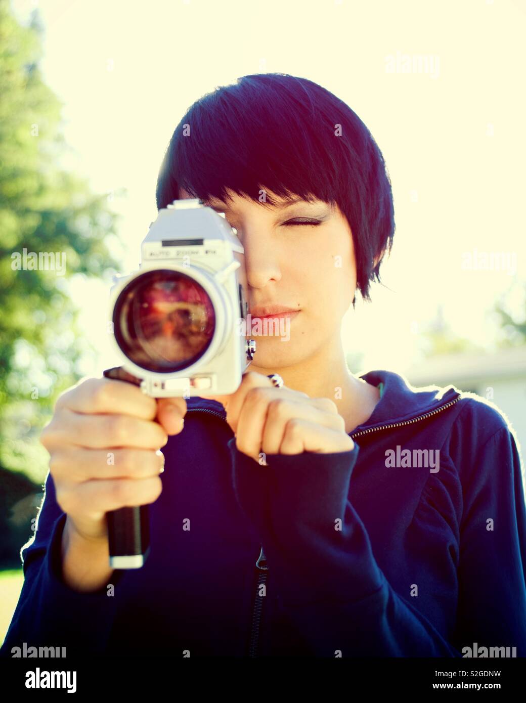 Jolie fille aux cheveux courts au début de la vingtaine tenant un vintage super 8mm à l'extérieur sur une journée ensoleillée. Photo a une couleur. processus croisés Banque D'Images