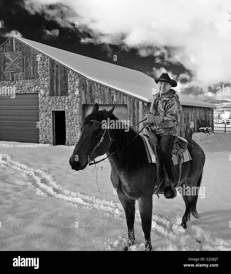Wyoming ranch équitation son cheval en hiver. La structure derrière lui, sa grange. Banque D'Images