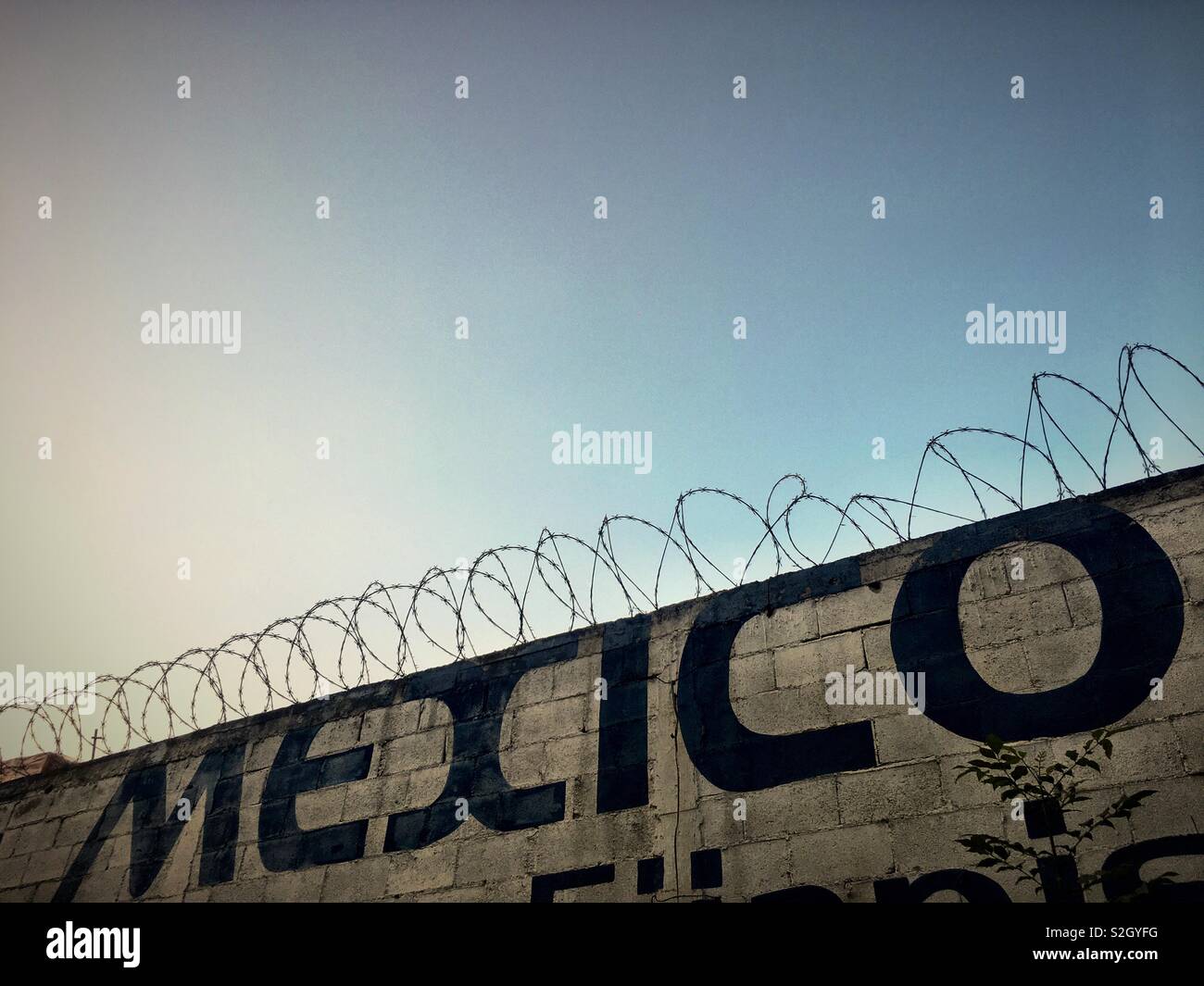 Photo de rue, mur commun avec Barb Wire et un Mexique peint sur parole. Pris avant le coucher du soleil, pas de nuages, mais un ciel couleur de la pollution. Banque D'Images