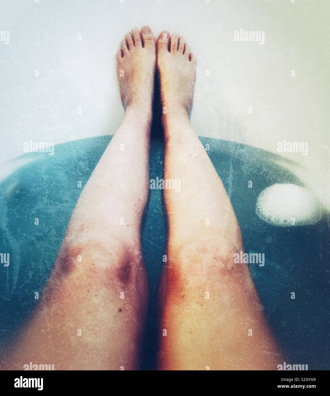 Les jambes dans une baignoire avec de l'eau bleue Banque D'Images