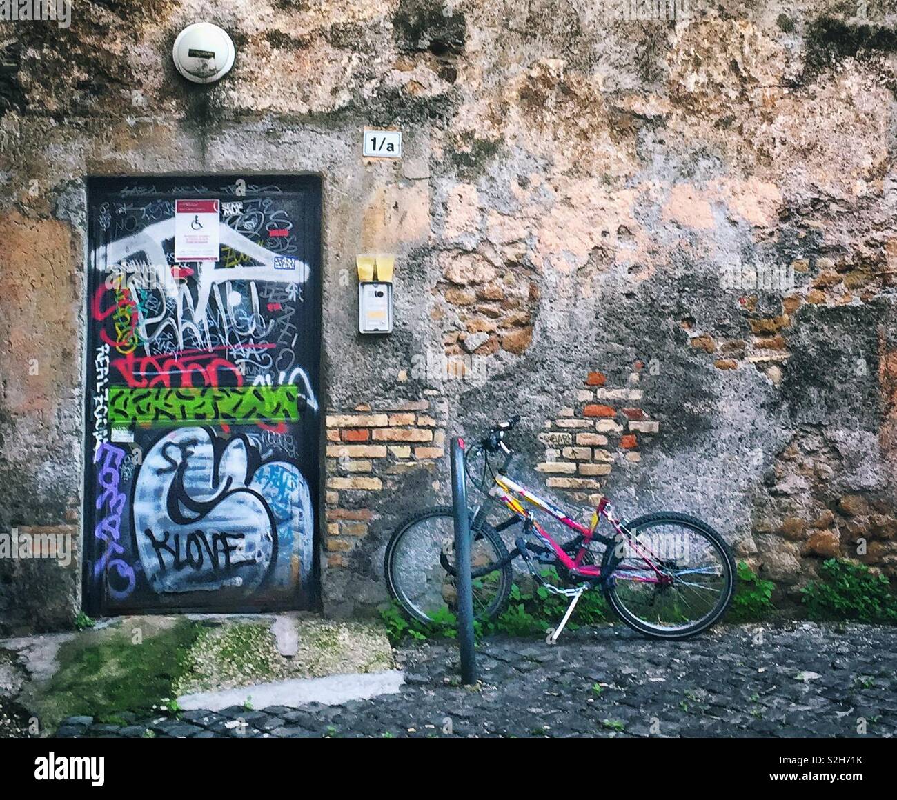 Location appuyé contre un mur à côté d'une porte couverte de graffiti - Image de stock capturée avec un smartphone
