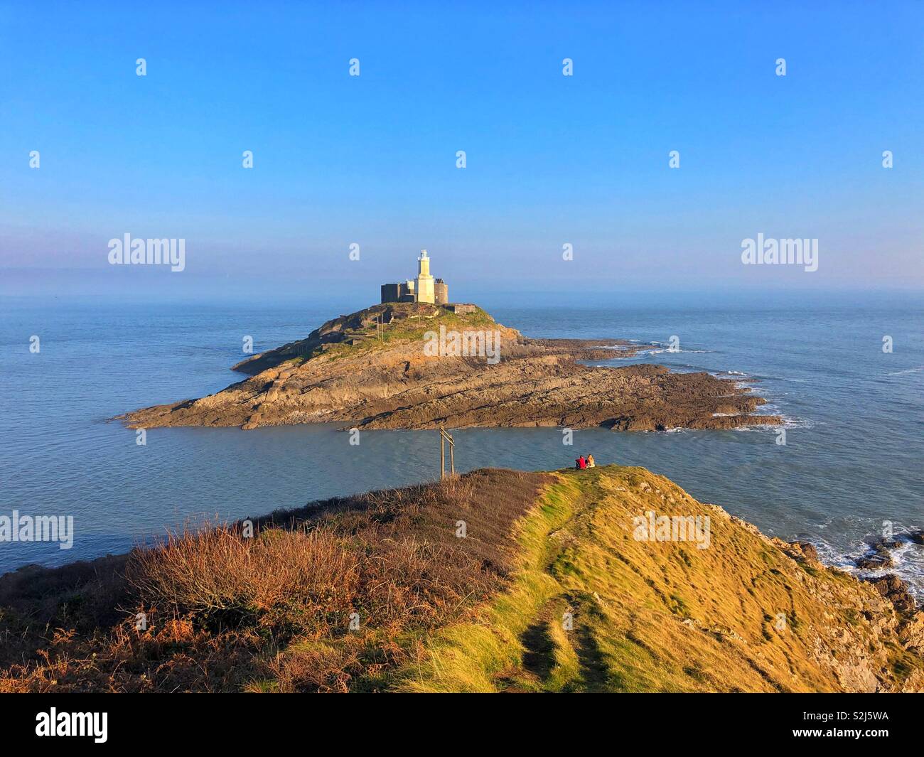 Jeune couple en profitant de la vue de Mumbles leuchtturm de Mumbles Pointe, La Baie de Swansea, Pays de Galles du Sud-Ouest, février. Banque D'Images