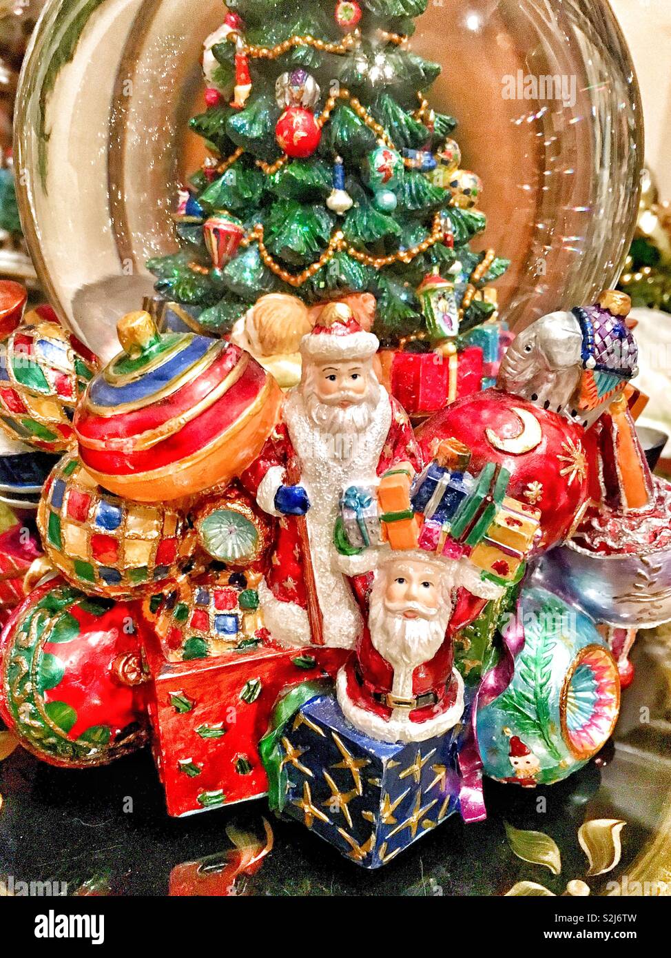 Snow globe avec l'arbre de Noël décoré et Santa figurines détenant plusieurs présente entouré d'ornements de Noël géant Banque D'Images