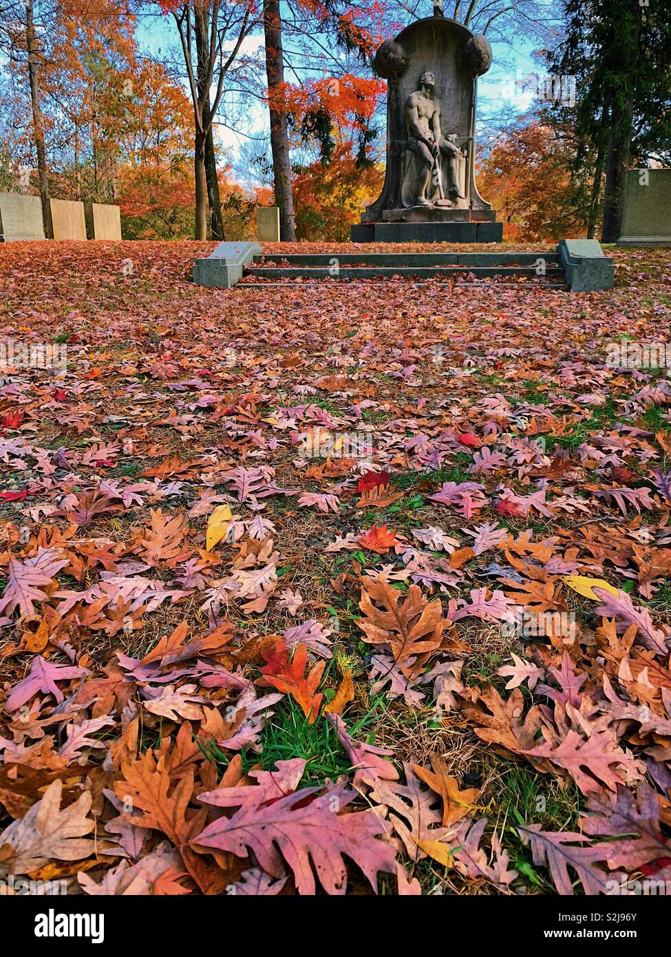 Statue de pierre tombale élaborée en arrière-plan avec des feuilles tombées rouges et oranges au premier plan. Le mémorial Henry villard par Karl Bitter. Situé au cimetière Sleepy Hollow à New York en automne. - Image de stock capturée avec un smartphone