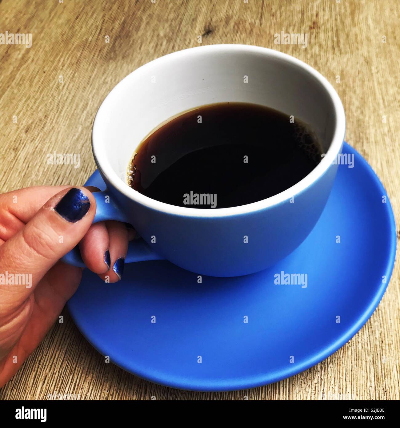 La main avec le bleu vernis à ongles sur les doigts, la tenue d'une grande tasse de café bleu Banque D'Images