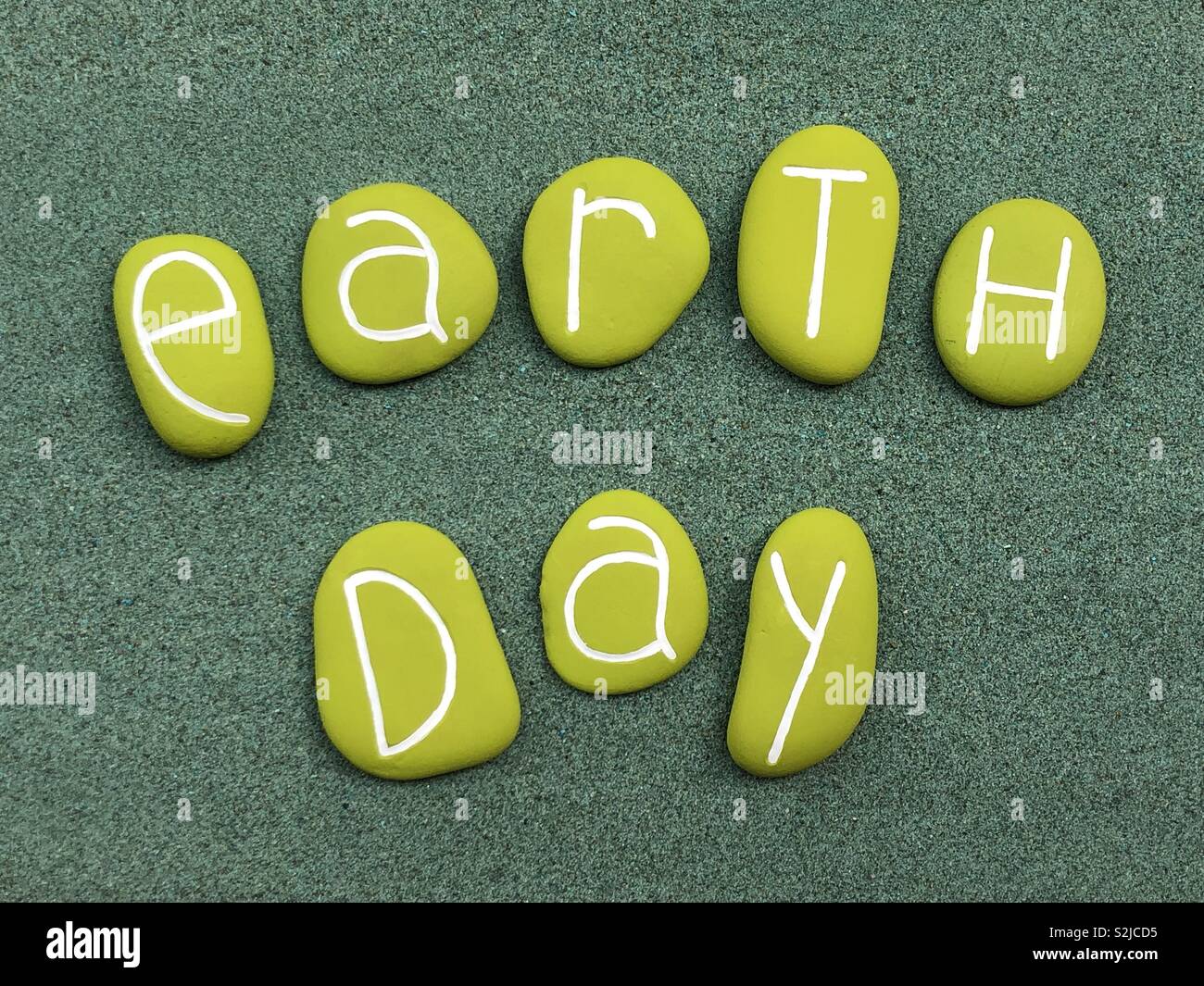 Le jour de la Terre célébré avec des pierres de couleur verte sur le sable vert Banque D'Images