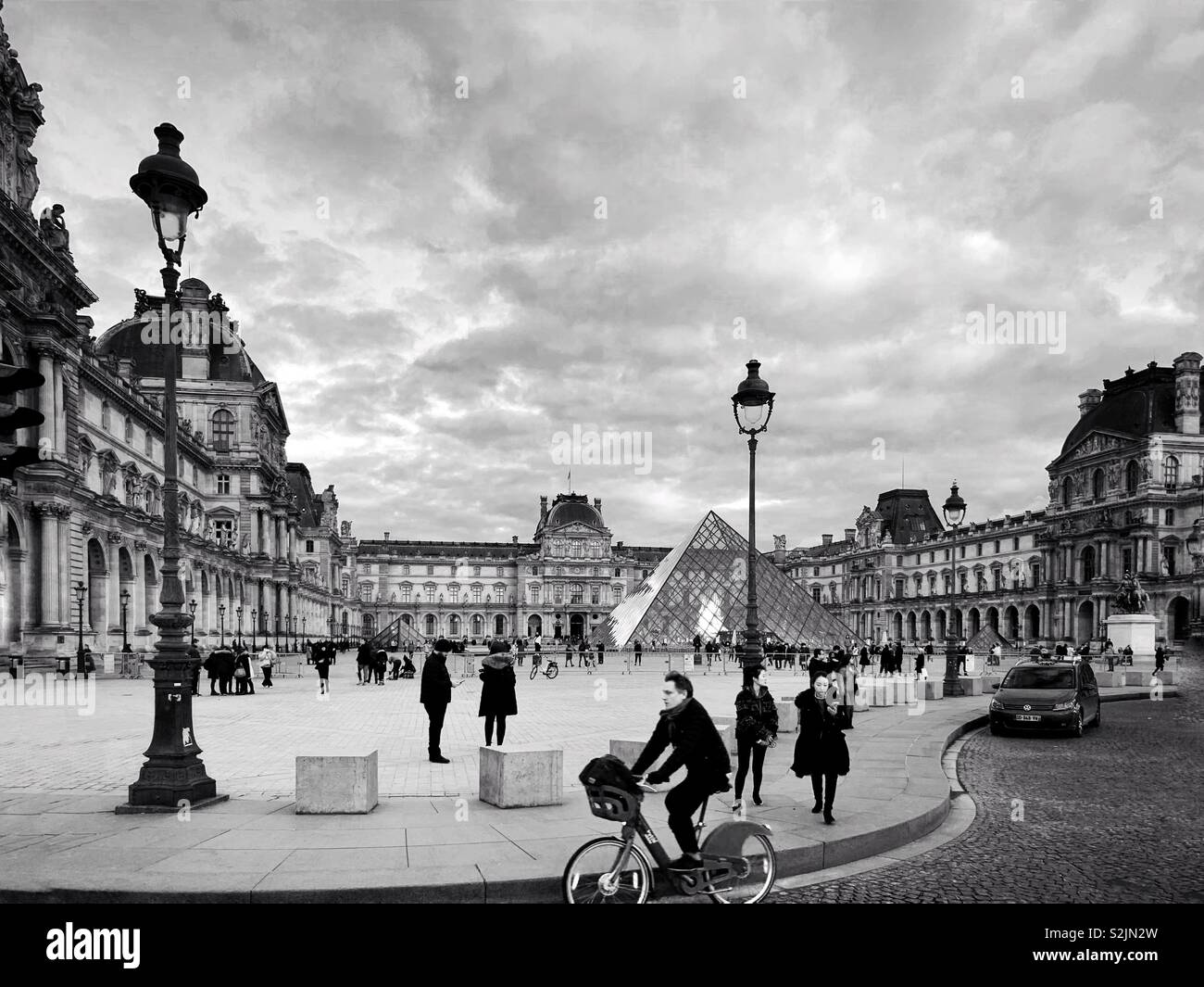 Un homme conduit une location et les touristes se tiennent près de la pyramide du Louvre à l'entrée du musée du Louvre à Paris, France - Image de stock capturée avec un smartphone
