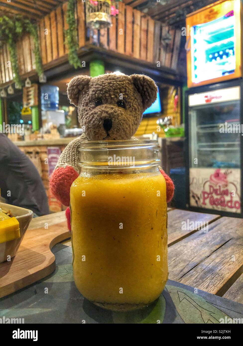 Une soif ours debout derrière un verre rempli de jus de mangue. Banque D'Images