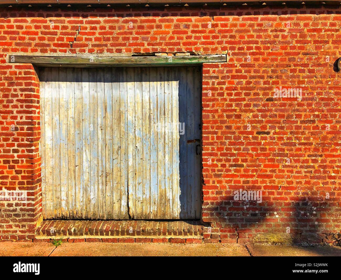La porte de garage avec l'écaillage de la peinture bleu pâle dans un mur de brique rouge. Banque D'Images