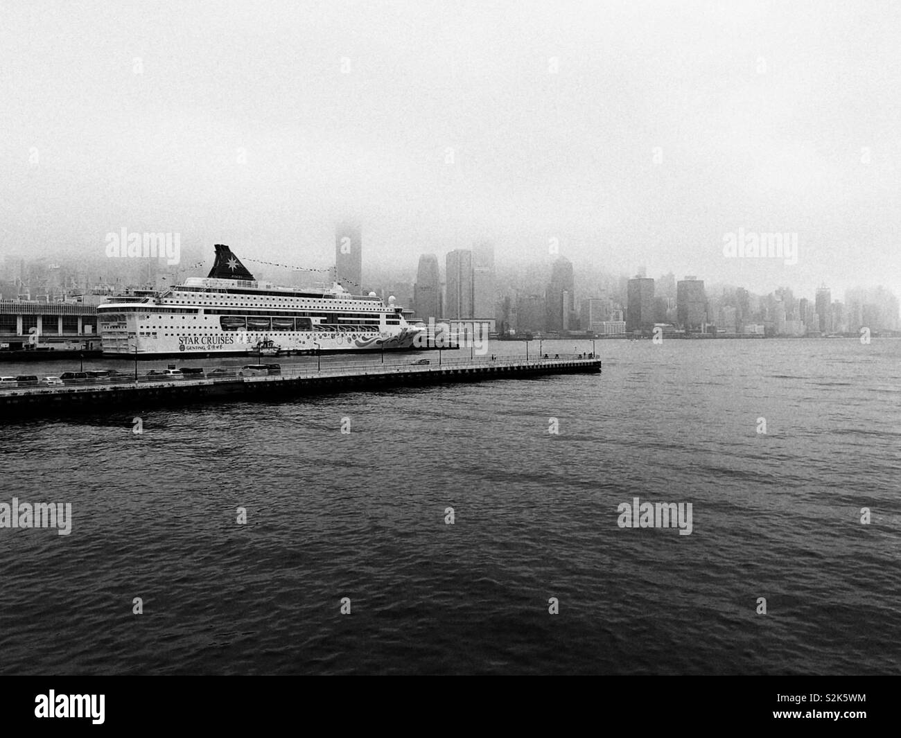 B&W photo de Victoria Harbour Hong Kong nuageux avec bateau de croisière par arrêt Banque D'Images