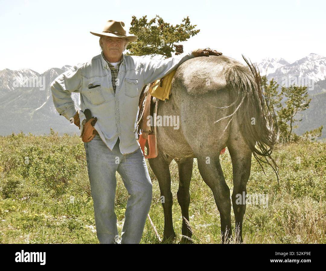 Un propriétaire de ranch du Wyoming posant avec son cheval dans les montagnes du Wyoming Grand Teton. Remarque sa main droite est sur son pistolet. Banque D'Images