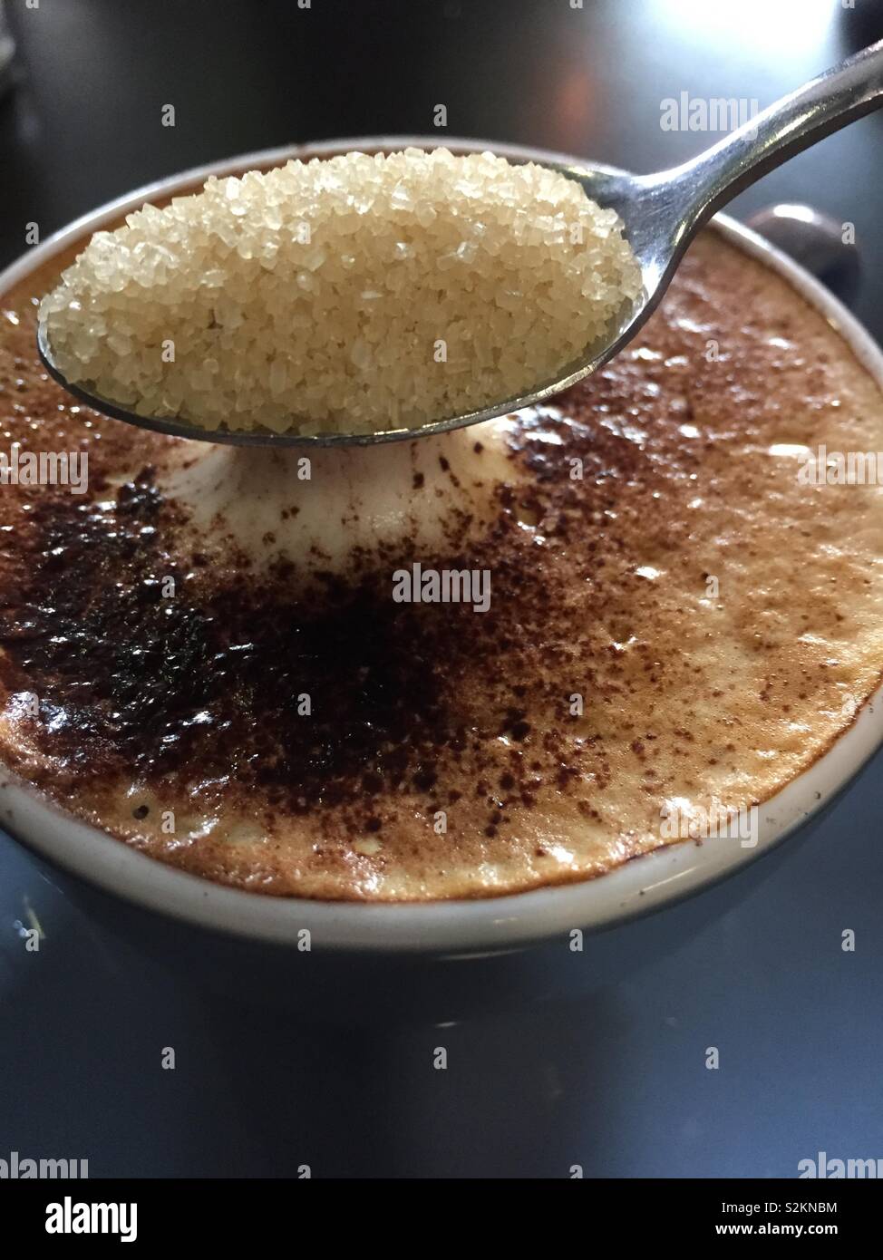 Une cuillère pleine de sucre soit ajouté à mousse tasse de cappuccino, libre. Arrière-plan de verticale libre du lait moussé boire dans une tasse de chocolat saupoudré sur le dessus Banque D'Images