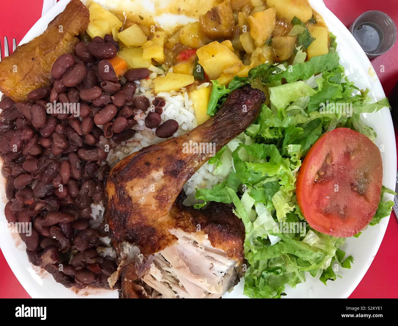 Un gros plan d'un déjeuner typique du Costa Rica complet avec du poulet rôti, haricots verts, salade verte, pommes de terre, et le plantain frit. Oops, quelqu'un a pris une bouchée du poulet ! Banque D'Images