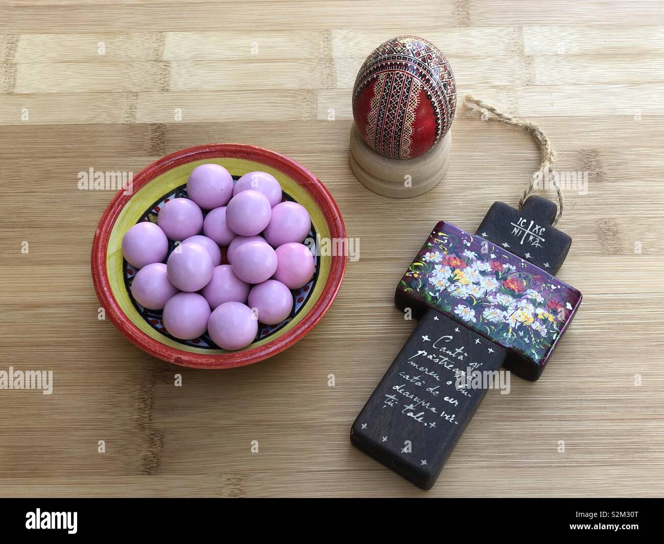 Temps de Pâques avec un oeuf décoré, une croix en bois et un bol en céramique avec chocolats rose Banque D'Images