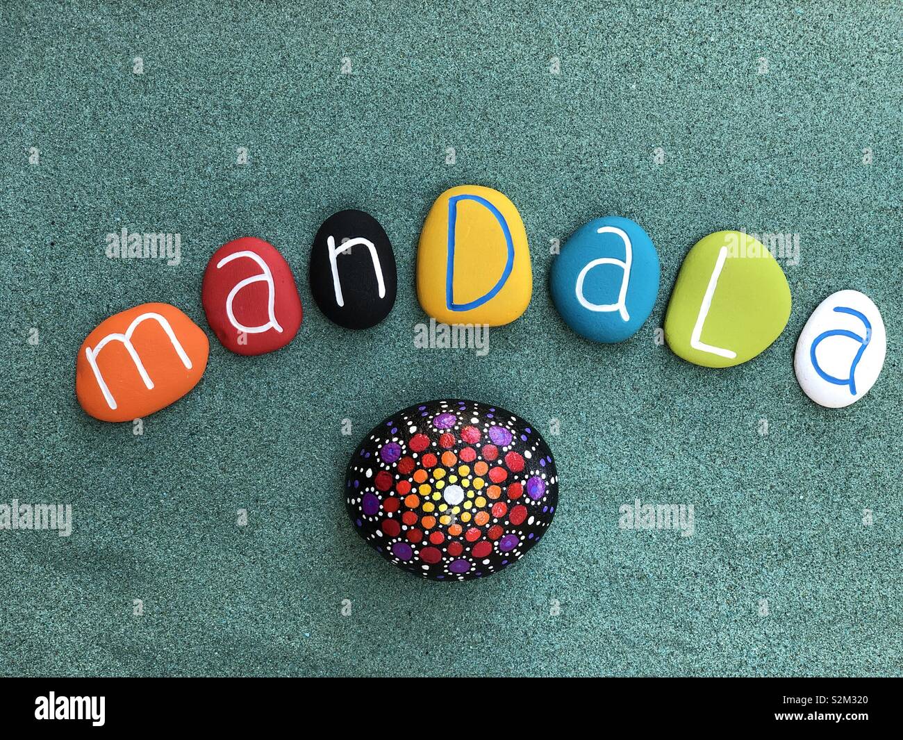 Mandala peint sur une pierre et du texte en couleur avec des pierres par-dessus la mer de sable vert - Image de stock capturée avec un smartphone