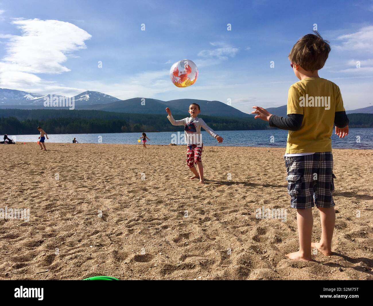 Garçons jouant avec ballon de plage sur la plage au bord du loch Banque D'Images