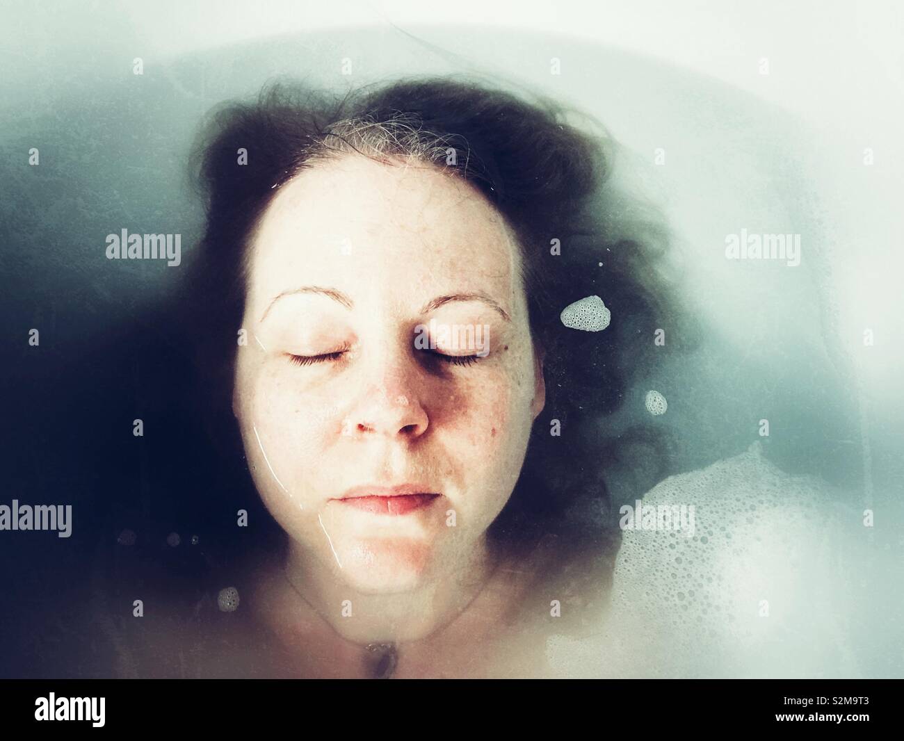 Young woman's face partiellement immergé dans un bain de mousse Banque D'Images