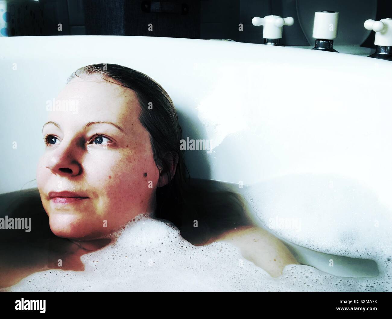 Femme dans un bain moussant à la recherche sur le côté Banque D'Images