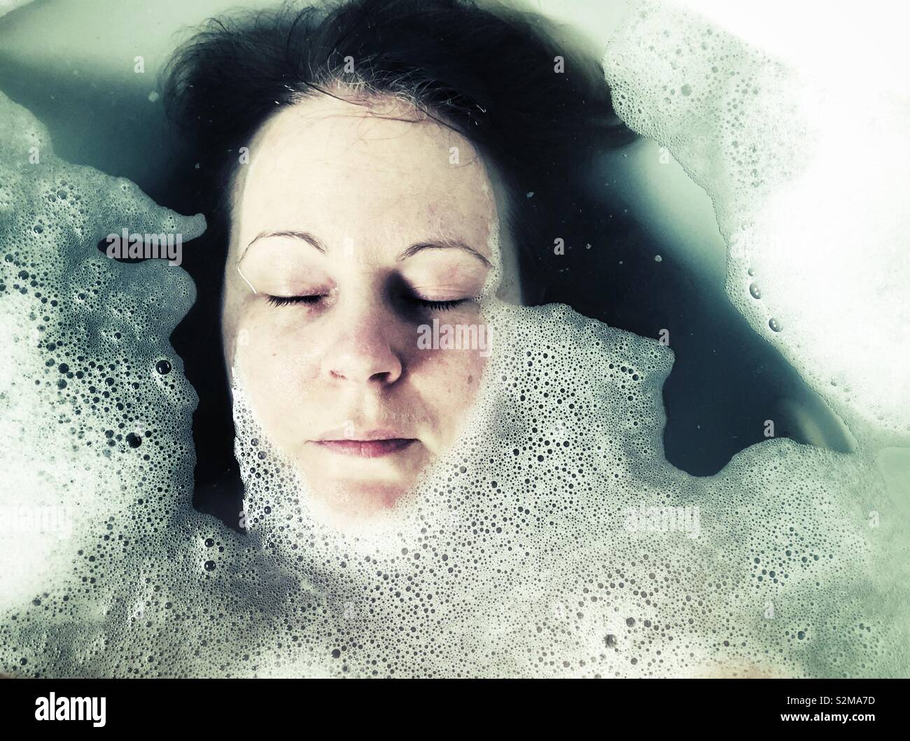 Visage de femme dans un bain de mousse avec les yeux fermés Banque D'Images