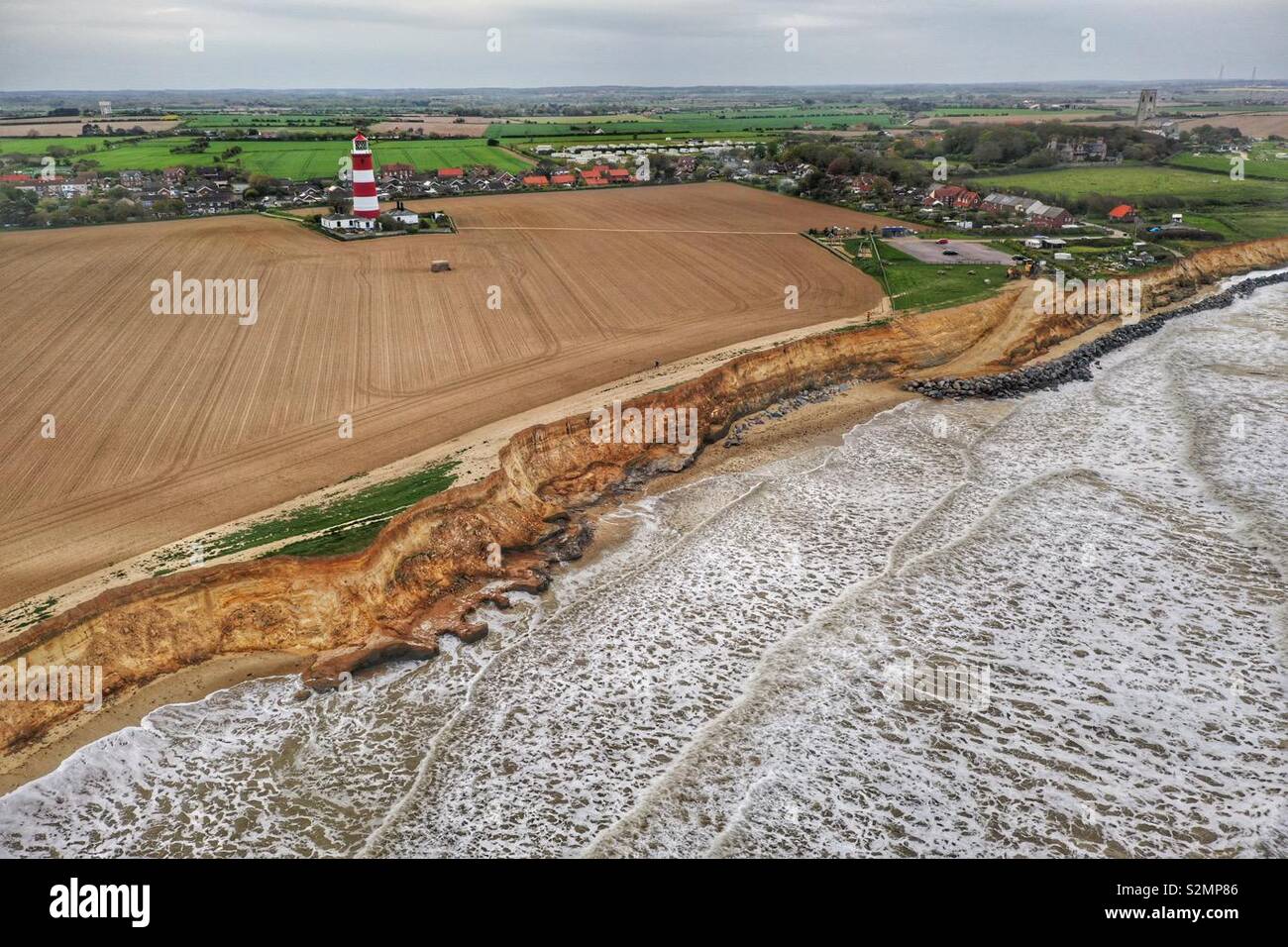 Photo aérienne de la falaise à Happisburgh à marée haute avec le phare, le village et l'église. - Image de stock capturée avec un smartphone