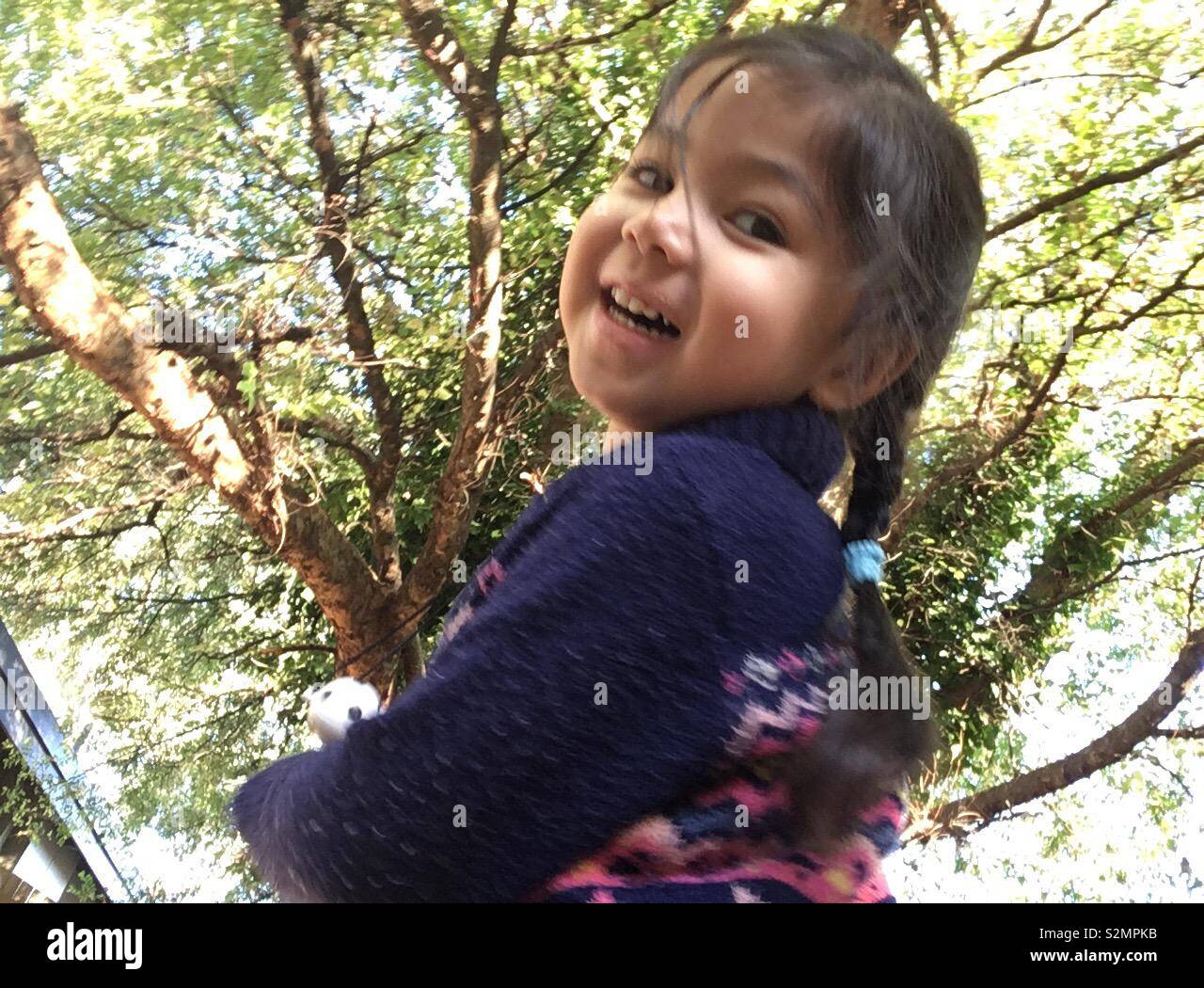 Jeune et mignon (Caucasien multi-ethnique/Punjabi/Vietnamien) girl heureusement jouer sous un grand arbre avec des feuilles vertes au cours d'une journée ensoleillée d'automne. Banque D'Images