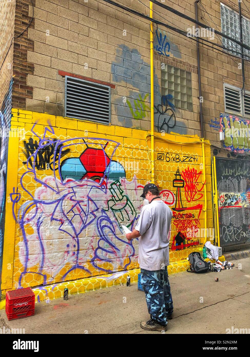 Un artiste de rue à l'œuvre dans l'écriture Graffiti Alley à Toronto, au Canada. - Image de stock capturée avec un smartphone