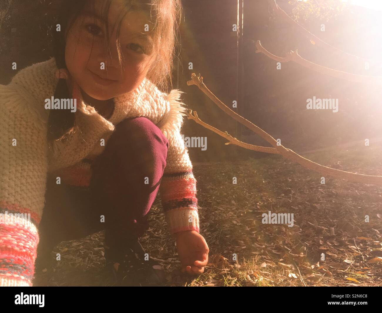 Un jeune multi-ethnique peau olive fille avec de longs cheveux brun foncé est jouer dehors pendant une après-midi ensoleillée d'automne en Australie. Elle porte une veste en tricot de coton et des jambières. Banque D'Images