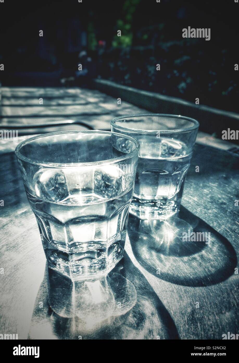 Partiellement deux verres d'eau clair plein soleil sur table de patio en métal avec des motifs de la réfraction et des ombres. - Image de stock capturée avec un smartphone