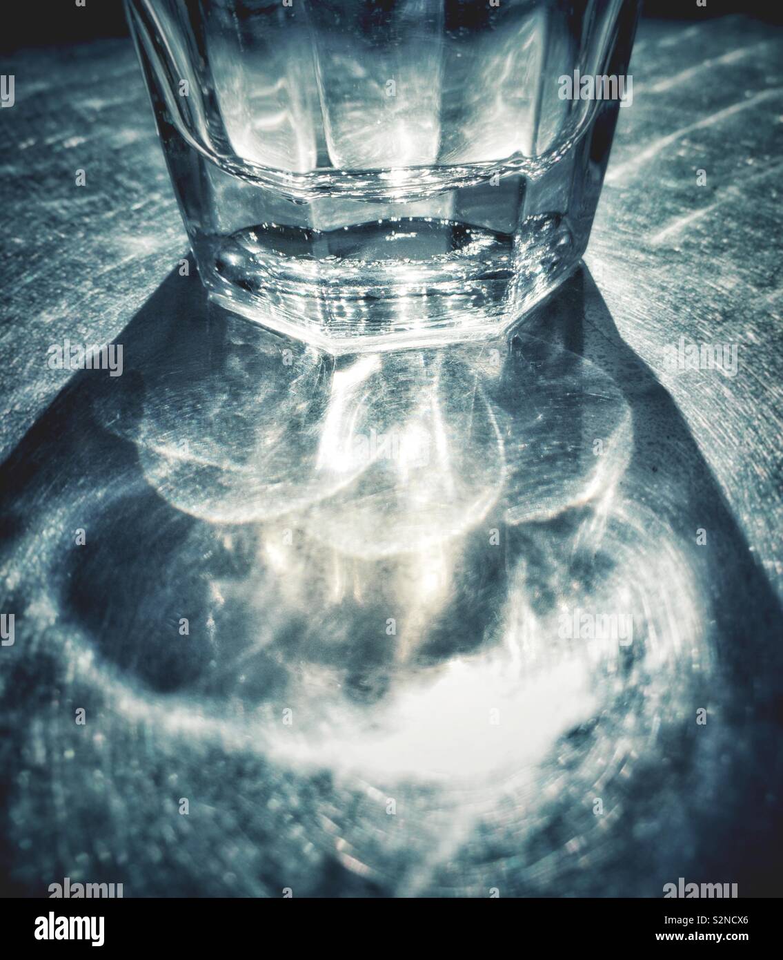 Résumé de verre plein d'eau partiellement ensoleillé sur table de patio en métal avec des motifs de la réfraction et des ombres. - Image de stock capturée avec un smartphone