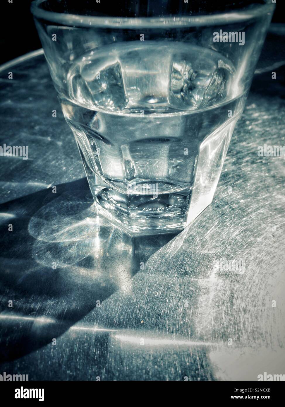Partiellement clair verre plein d'eau sur la table de patio en métal en plein soleil à l'extérieur en milieu urbain. - Image de stock capturée avec un smartphone