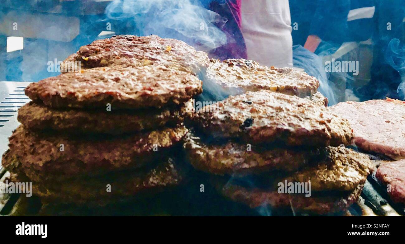 Burgers de boeuf empilés sur la grille chaude du barbecue en plein air Banque D'Images