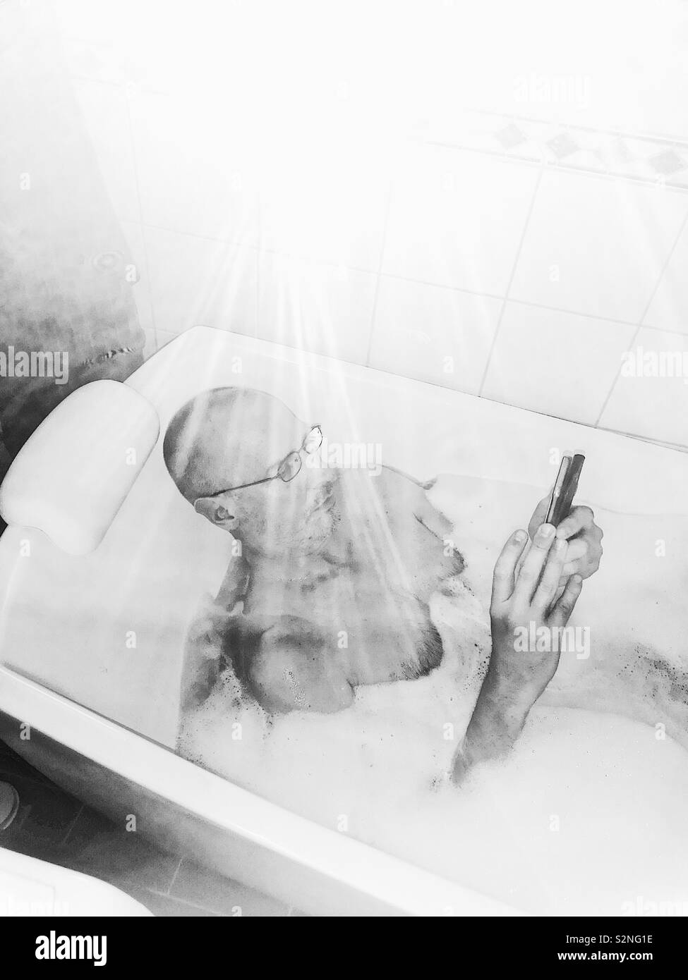 Handsome middle aged man using smartphone suédois dans la baignoire pleine de mousse Banque D'Images