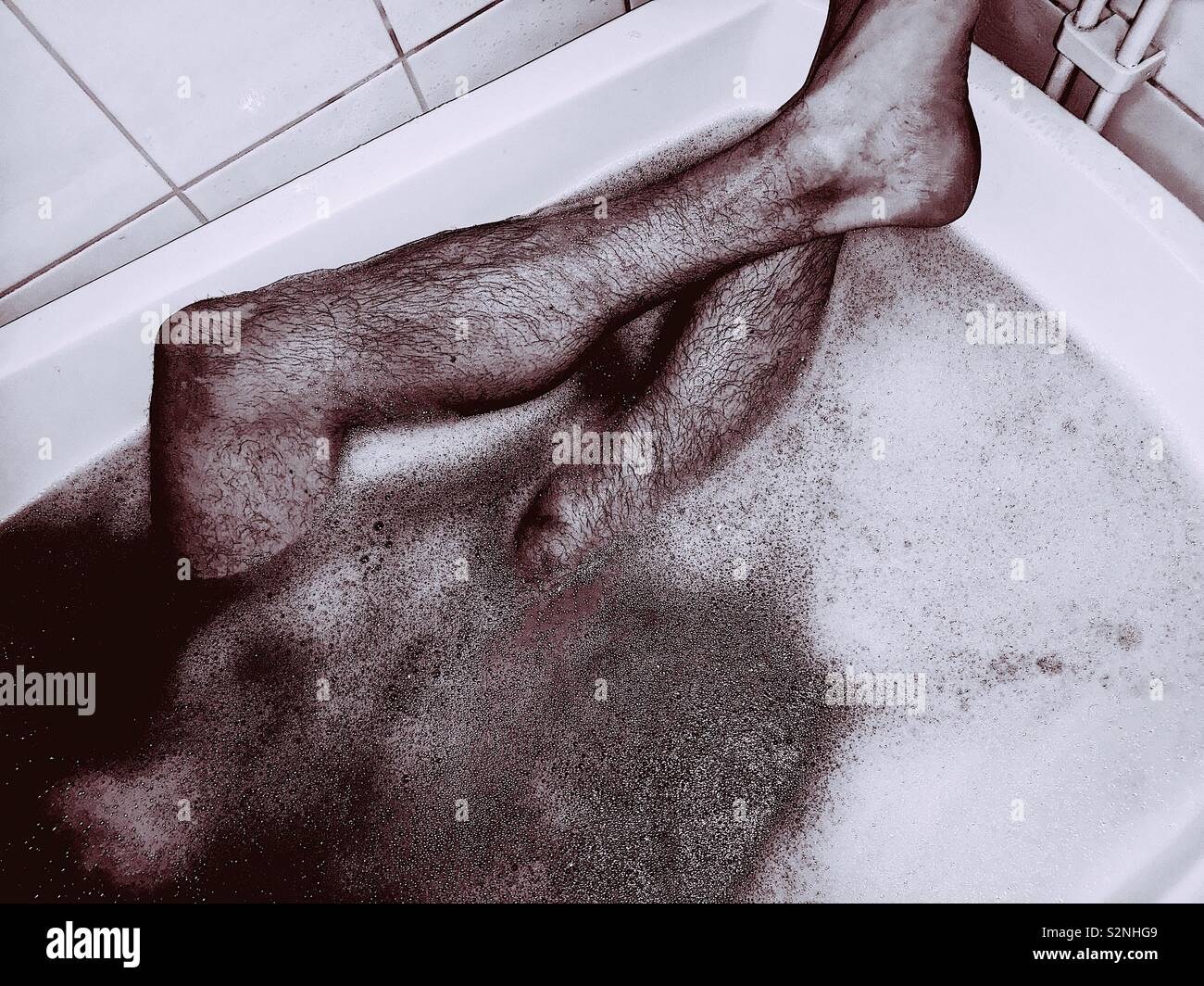 Jambes poilues mans en relaxant avec de la mousse de bain Banque D'Images