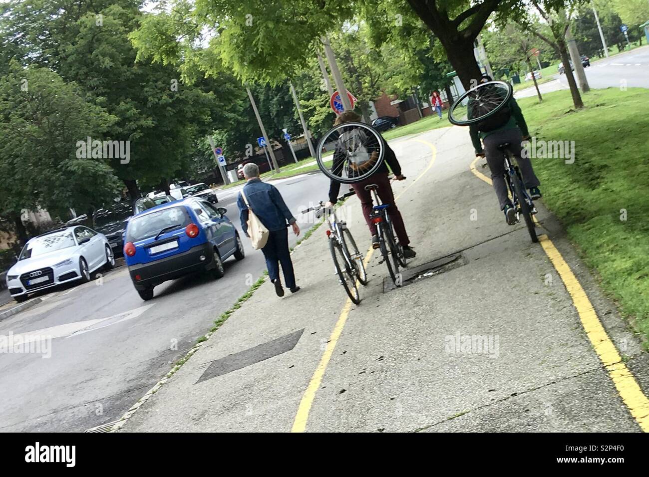 Modes de transport parallèles dans la rue : la conduite, la marche et le vélo. Les cyclistes transportant des roues de vélo sur le dos. - Image de stock capturée avec un smartphone