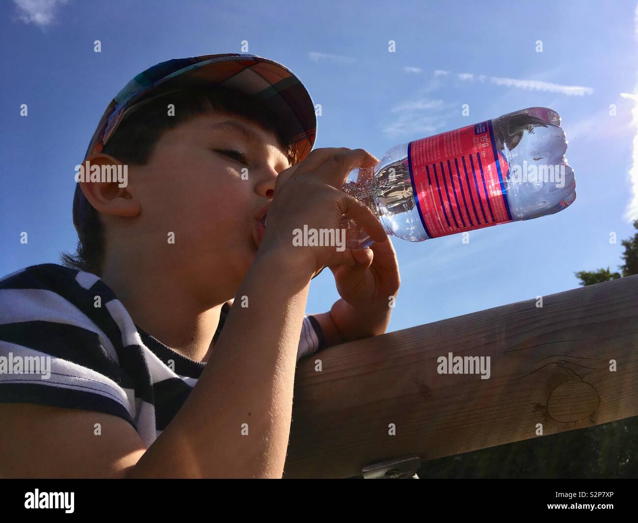 Enfant boire de l'eau minérale against blue sky low angle view Banque D'Images