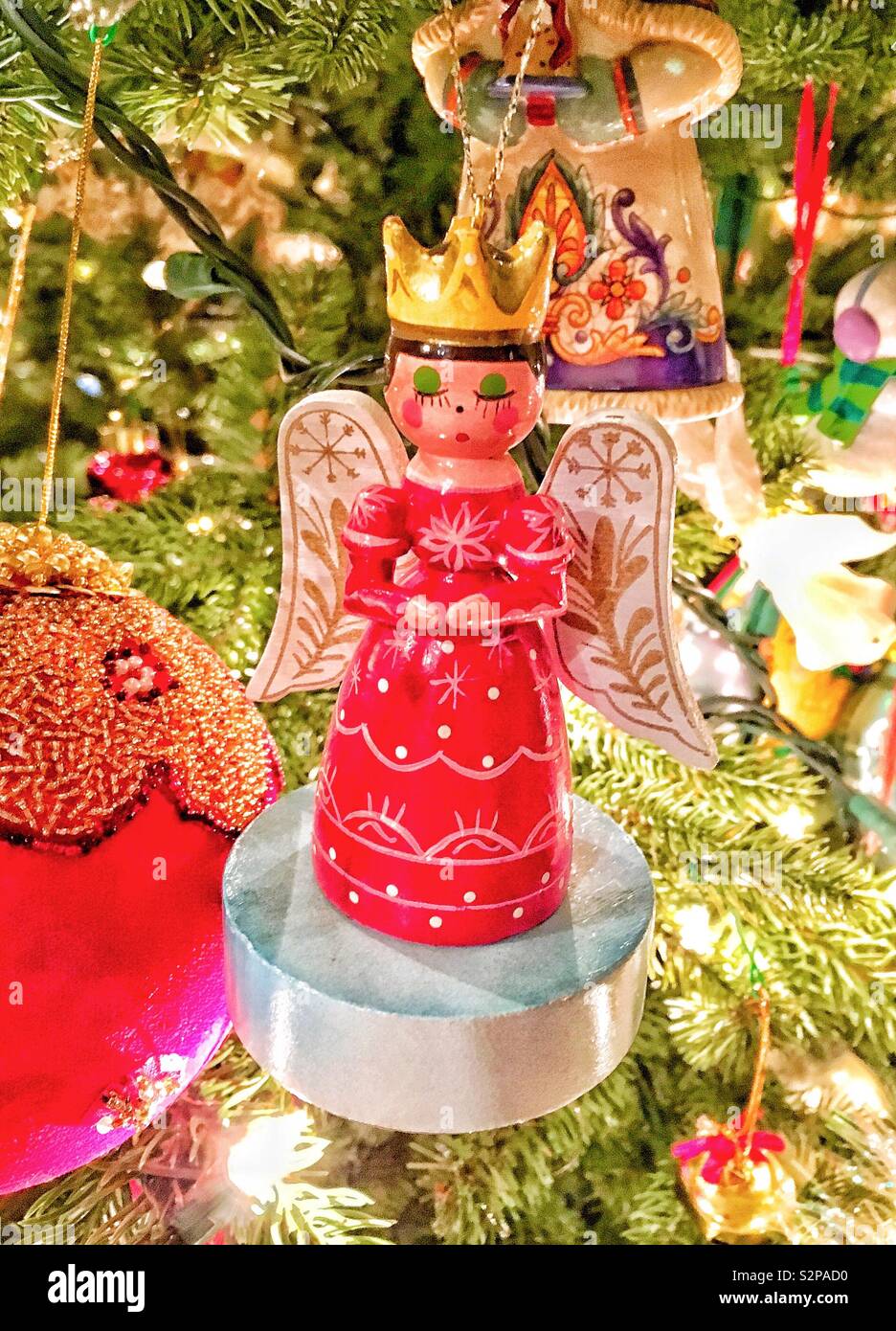 Ange en bois ornement en robe rouge portant la couronne d'or priant sur arbre de Noël entouré d'autres ornements et les aiguilles de pin Banque D'Images
