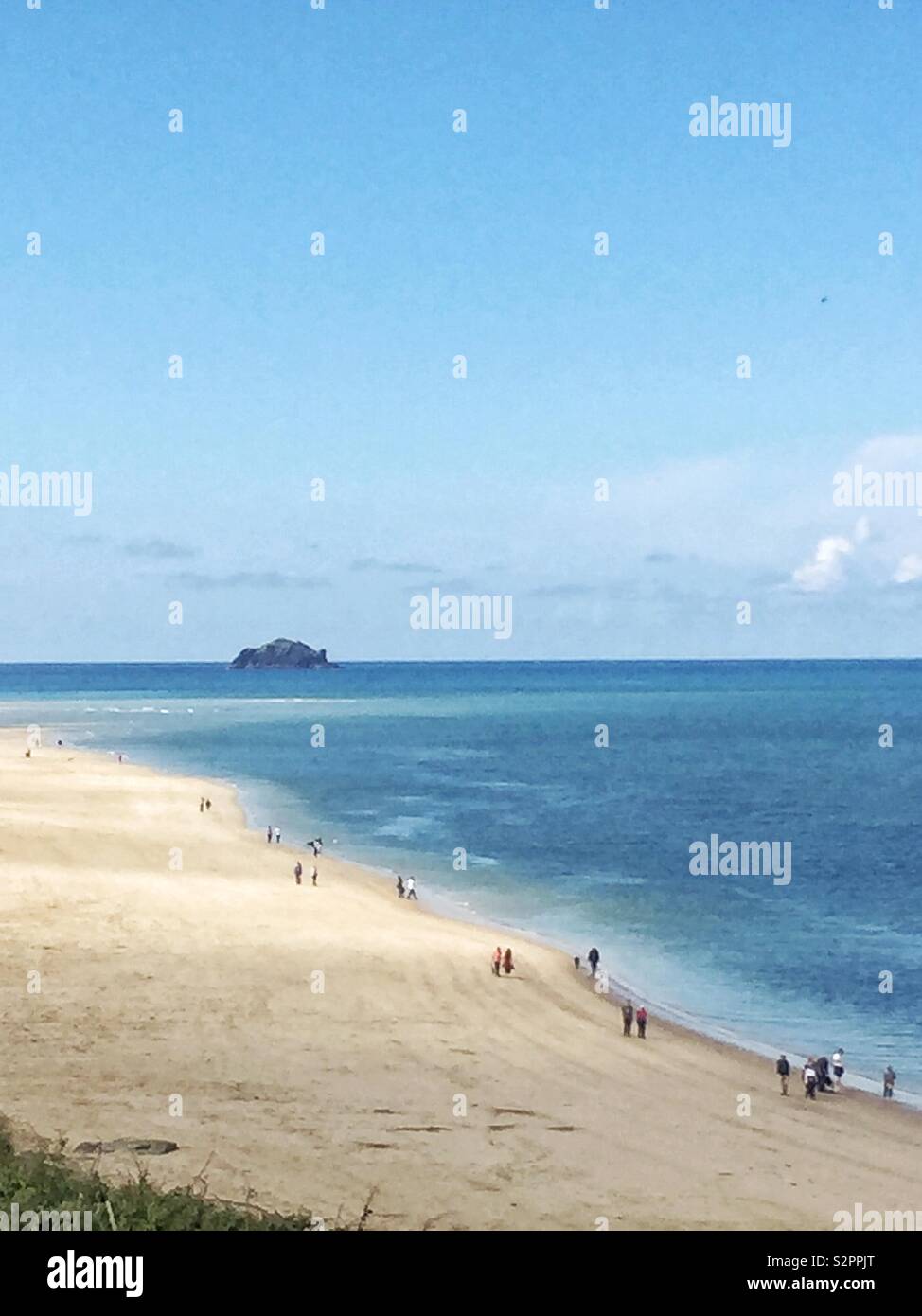 Une vue à longue distance d'une plage de sable blanc sur une île tropicale avec des gens qui marchent le long de la côte d'un océan bleu et calme à Cornwall - Image de stock capturée avec un smartphone