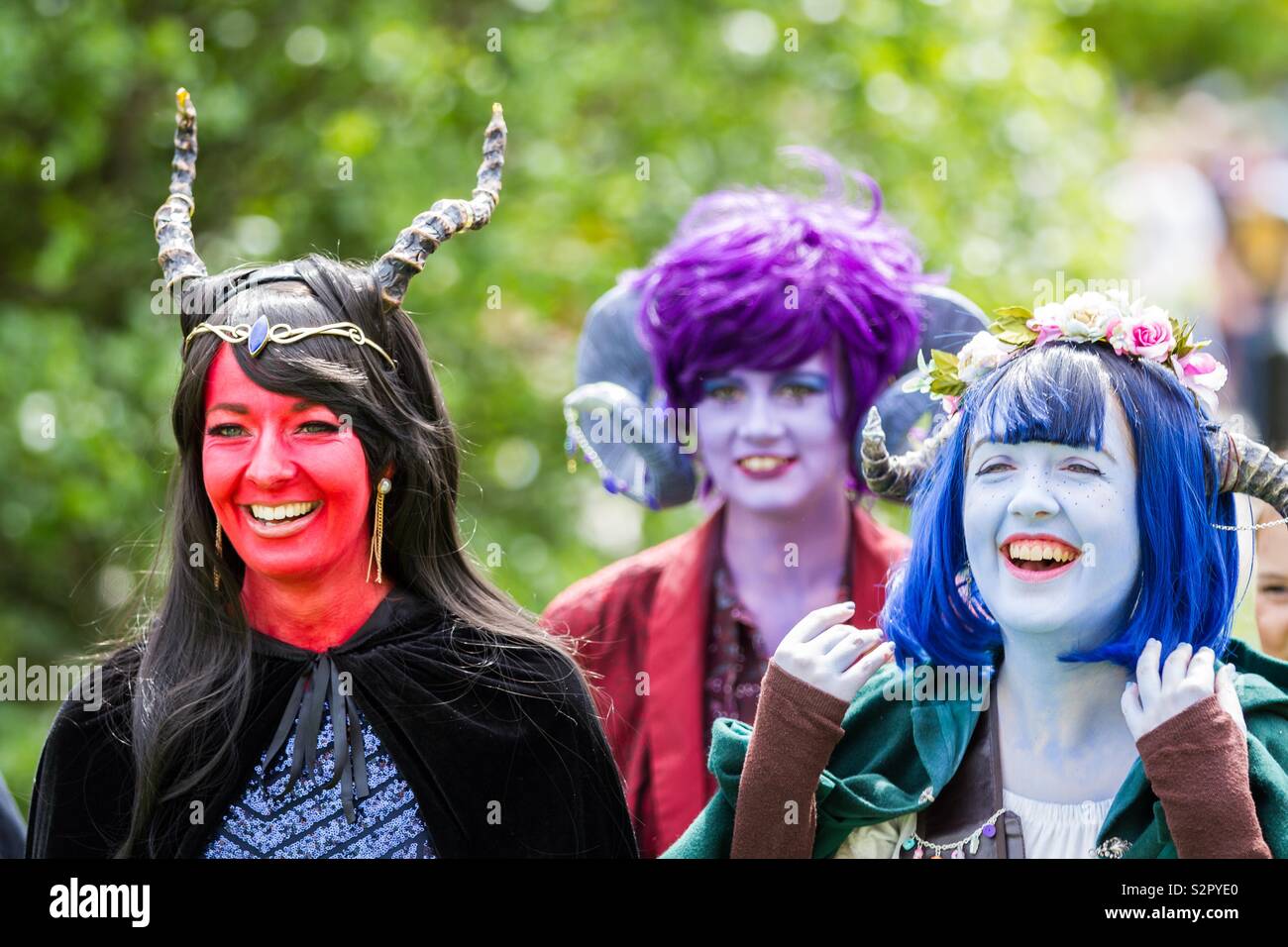Un groupe de filles de cosplay habillés comme des créatures avec la peinture pour le visage coloré et les perruques rire ensemble dans un portrait candide à un événement comic con Banque D'Images