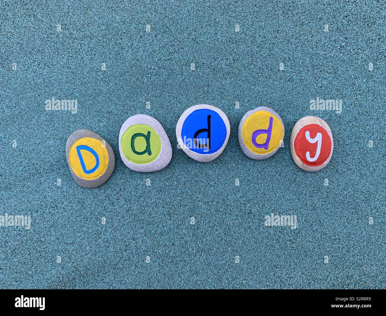 Papa, le jour de père célébré avec une composition de galets de couleur créative plus de lettres de sable vert - Image de stock capturée avec un smartphone