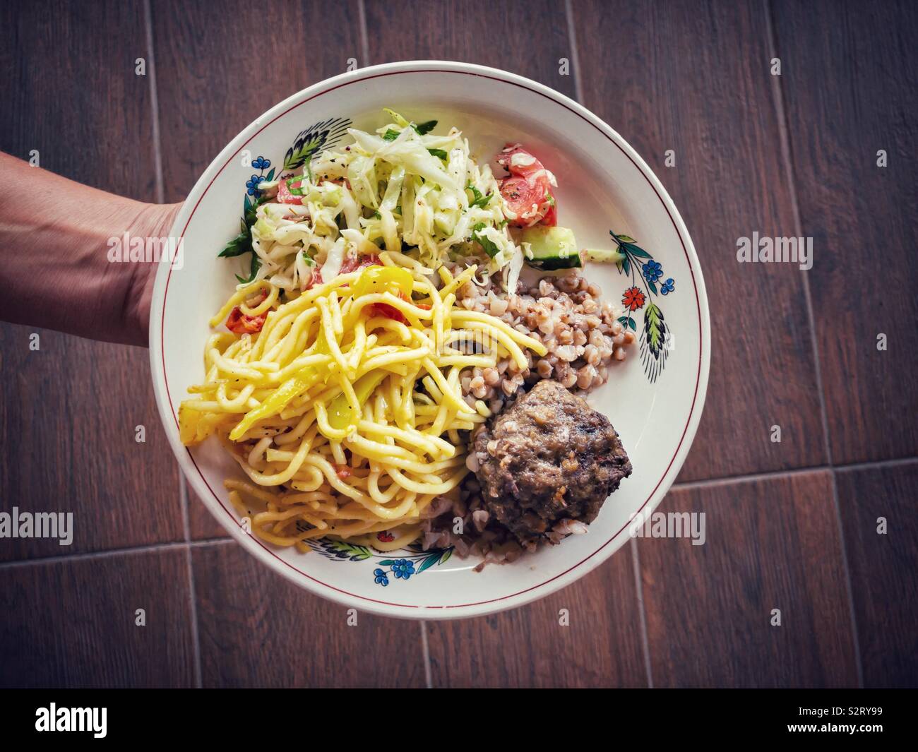 En tenant la main assiette pleine de nourriture - une salade de légumes, de sarrasin, spaghetti, escalope Banque D'Images
