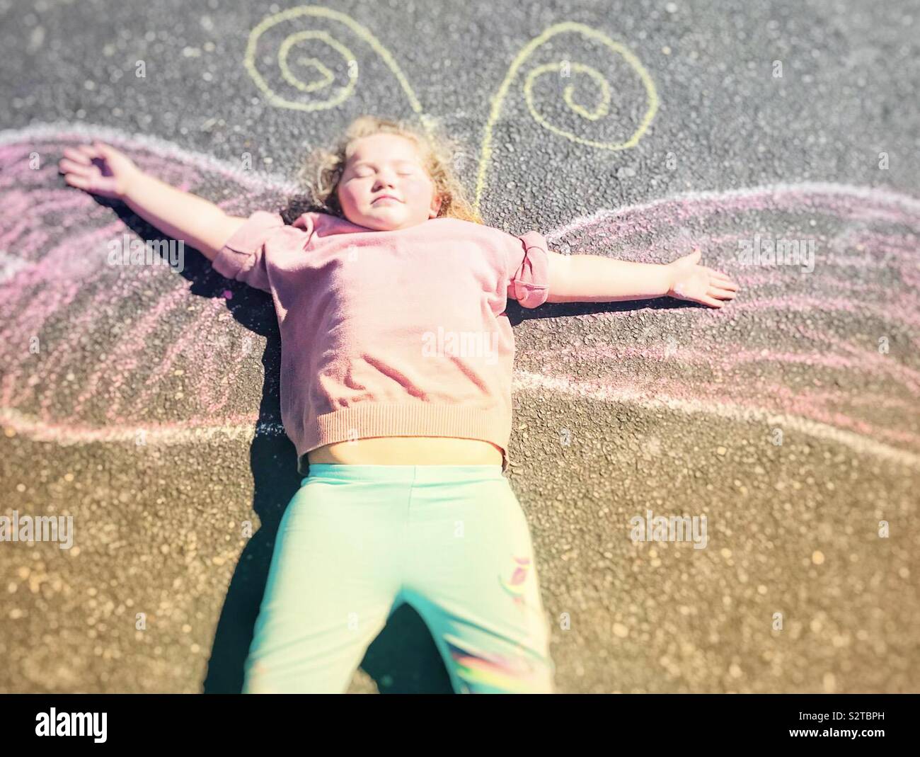 Petite fille qui met sur un dessin à la craie de papillon Banque D'Images