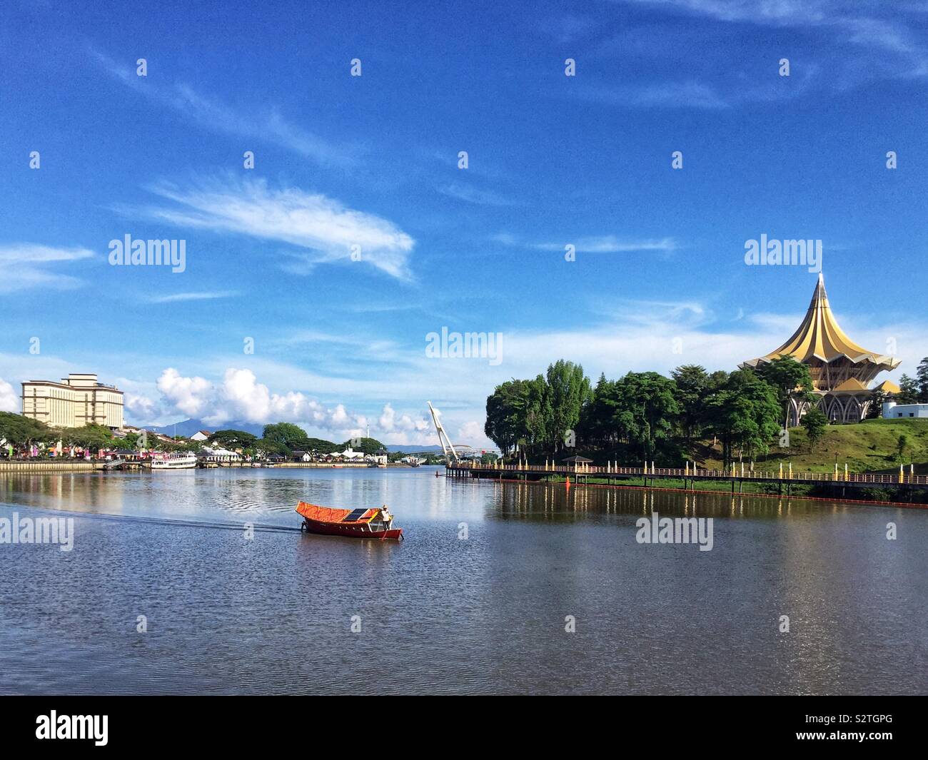 Un sampan malais traditionnel est utilisé pour transporter des personnes à travers la rivière Sarawak du bord de l'enceinte parlementaire sur la rive sud, avec l'Édifice de l'Assemblée législative de l'État, Kuching, Sarawak, Malaisie - Image de stock capturée avec un smartphone